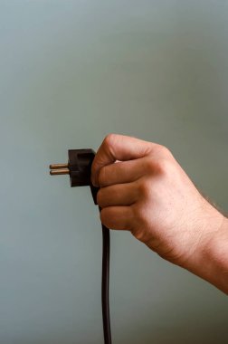 Elinizde bir elektrik prizi var. Siyah elektrik kablosu ve soketi olan bir adamın sol eli. Kafkasyalı, 43-45 yaşlarında. Elektrik güvenliği.