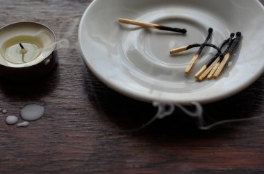 Tahta bir masada kararmış küçük bir mum. Masadaki balmumu kameraların ve beyaz bir tabakta yanmış kibritlerin yanında..