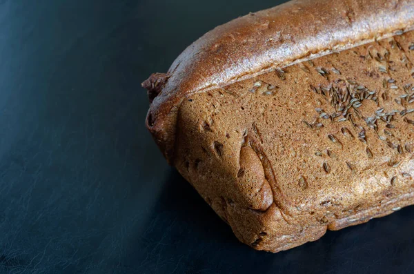 Bir somun çavdar ekmeği ve siyah arka planda karanfil tohumu. Yanında taze ev yapımı kimyon tohumu serpiştirilmiş ekmek. Uzayı kopyala Seçici odak.
