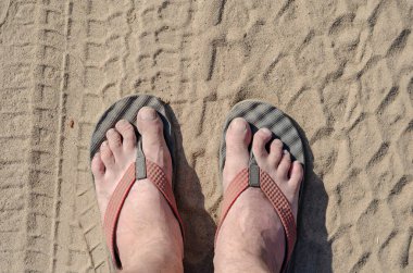 Terlik giymiş erkek bacaklarının üst görüntüsü. Çıplak ayaklı terlik giymiş olgun bir adam tozlu bir yolda duruyor. Ayakları toprak ve tozla kaplı.