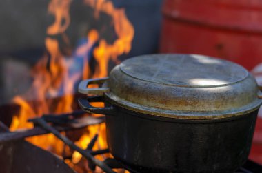 Kapağı yanan demir bir kazan dökün. Ateşin üstünde yemek pişirmek. Aktif dinlenme ve turizm. Yan görüş. Seçici odak.