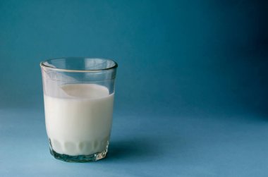 Cam bardak. Mavi arka planda kefir var. Bir bardak mayalanmış süt içeceği. İçmek sindirime iyi gelir. Boşluğu kopyala.
