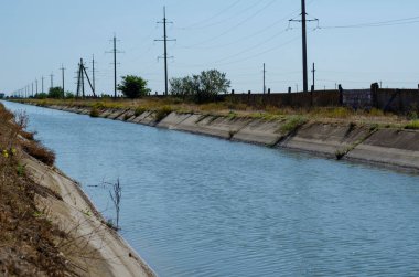 Suyla tarımsal kanallar sulanıyor. Kanal boyunca sulama için elektrik hattı var. Yaz güneşli bir gün. Tarım işi. Seçici odak.
