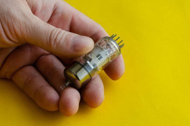 Erkek el sarı arka planda vakum tüpü tutuyor. Operasyondan bir erkeğin elinde çıkan bir telsiz tüpü. Radyo parçaları toplamak ya da geri dönüşüm yapmak. Seçici odak.