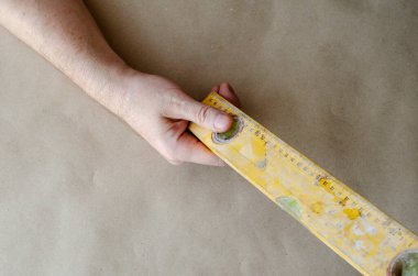 Yetişkin bir beyaz adamın elinde sarı bir inşaat katı var. Çizikler ve çimento izleri olan gerçek bir el aleti. İnşaat endüstrisi. Seçici numara.