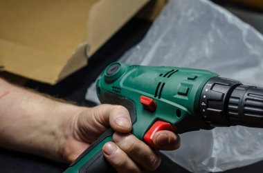 Erkek eller eşyalarınızı çıkarın ve elektrikli matkabı inceleyin. Yetişkin bir adam internetten satın alınmış elektrikli bir aleti inceliyor. Seçici odaklanma. Bir serinin parçası