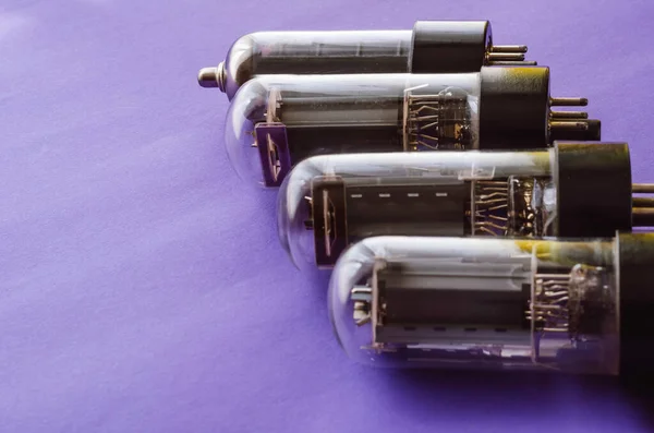 Four vacuum tubes on a blue background. Outdated radio tubes. Vintage radio parts. Selective focus.