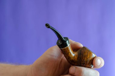 Elinde dumanlı pipo var. Mavi arka planda klasik bir sigara piposu tutan bir adam. Seçici odak.