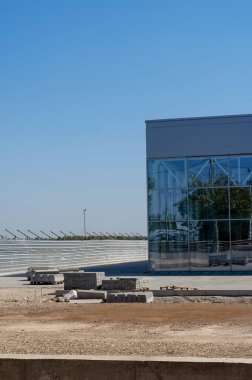 Cam ve betondan yapılmış inşaat halindeki bir şirket binasının ön cephesi. Ticari gayrimenkullerin tamamlanmamış inşaatı. Çimsiz çimenlik. Güvenlik kamerasıyla park etmek..