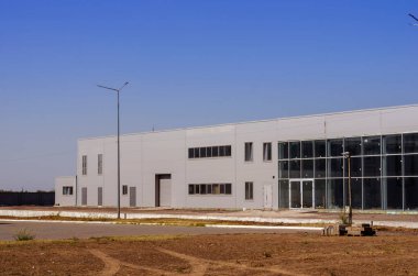 Cam ve betondan yapılmış inşaat halindeki bir şirket binasının ön cephesi. Ticari gayrimenkullerin tamamlanmamış inşaatı. Çimsiz çimenlik. Güvenlik kamerasıyla park etmek..