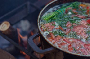 Balık çorbası domates ve dereotu ateşte pişiriliyor. Doğada demir bir kasede taze çorba. Etkin yaşam biçimi.