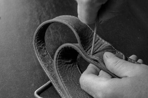 A man makes holes in a leather collar with an awl. Hands of an adult man with a metal awl and a wide collar. Pet equipment repair. Selective focus.