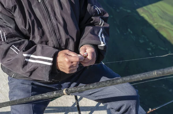75歳の男性はフックから小さな魚を削除します 拳でキャッチとしわの手のクローズアップ 高齢者の積極的なライフスタイル 選択的焦点 — ストック写真