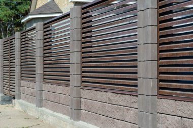 Gri taş kolonları olan kör çitler. Kulübenin etrafında kahverengi bir çit var. Özel mülk. Köy köyü.