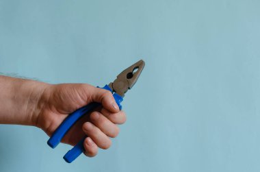 Mavi dielektrik kabzalı pense erkek elinde. Bir adamın eli bir elektrikçinin aletini tutar. Avrupa ırkının orta yaşlı adamı. El aracı.