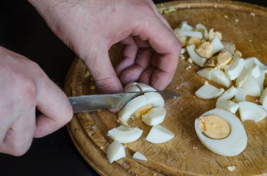 Erkek eller, tahtadan kesilmiş bir tahta üzerinde haşlanmış tavuk yumurtası. Olgun adam yemek pişirir. Seçici odak.