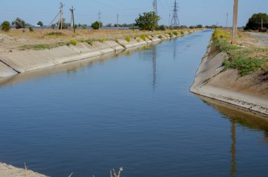 Suyla tarımsal kanallar sulanıyor. Kanal boyunca sulama için elektrik hattı var. Yaz güneşli bir gün. Tarım sektörü.