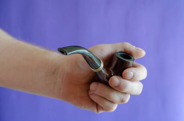 Elinde dumanlı pipo var. Mavi arka planda klasik bir sigara piposu tutan bir adam. Seçici odak.