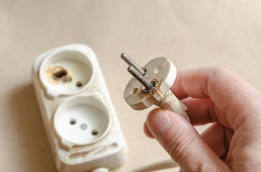 Bir elektrikçi bir elektrik prizinin yandığını gösteriyor. Erkek eli kısa devreden sonra beyaz uzatma kablosu. Elektrik güvenliği.