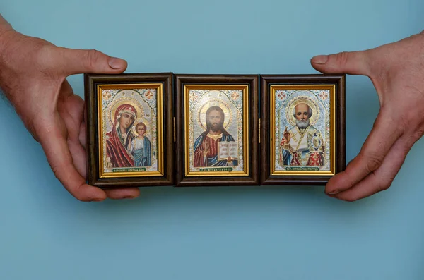 Hands hold the Christian icon of Christ, the mother of God and St. Nicholas the wonderworker, the patron saint of sailors and travelers. The inscriptions in the Old Slavonic language mean the names of those depicted on the icon. Orthodox Church.