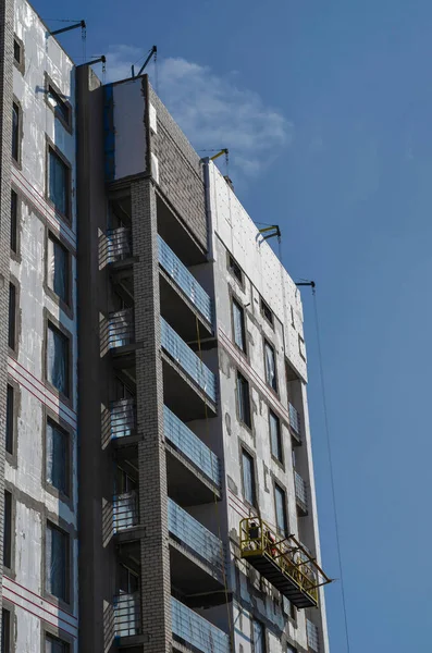 An unfinished skyscraper building against the blue sky. Facade works on heat and moisture insulation of the outer walls of the building. Construction industry.