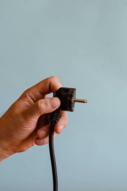 Elinizde bir elektrik prizi var. Siyah elektrik kablosu ve soketi olan bir adamın sol eli. Kafkasyalı, 43-45 yaşlarında. Elektrik güvenliği.