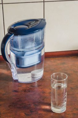 Su arıtma için bir sürahi ve mutfak masasında bir bardak..