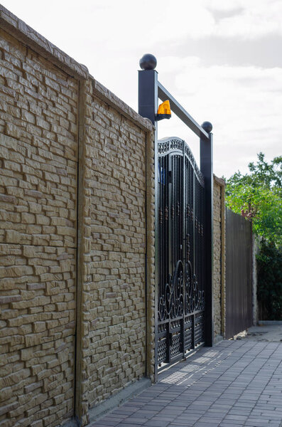 Beautiful stone fence of a country cottage. High railing with forged metal gates. Private property.