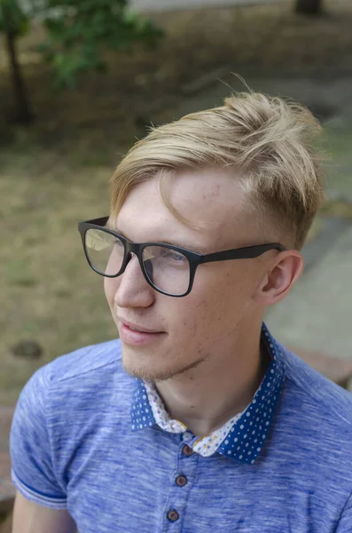 一个戴眼镜的时髦年轻人的画像 一位年轻英俊的男子 戴着时髦的眼镜 留着时髦的发型 穿着时髦的蓝色衬衫 站在街上 生活方式 — 图库照片