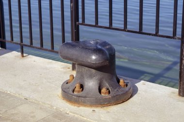 Beton iskelede büyük siyah bir kazık. Büyük gemileri, feribotları, tekneleri bağlamak ve demirlemek için tasarlandı. Kapat.