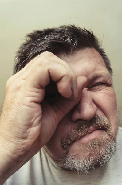 Unusual portrait of a man showing a peeping gesture. A grown man with a beard put his hand to his eye. Facial expressions and emotions.