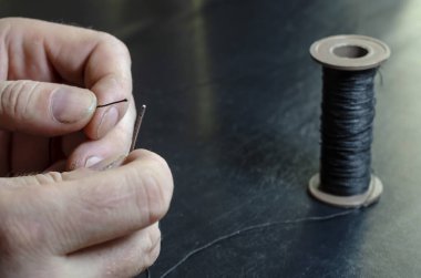 Adam ipliği iğnenin deliğine sokuyor. Elinde iplik ve iğne olan yetişkin bir adamın elleri. Terzi işi. Seçici odak.