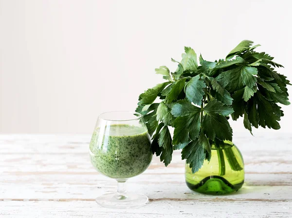 Green celery smoothie in a glass over white wooden background, front view.