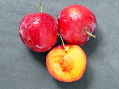 Koyu arka plan üzerinde su damlaları ve erik dilimleri ile Taze erik