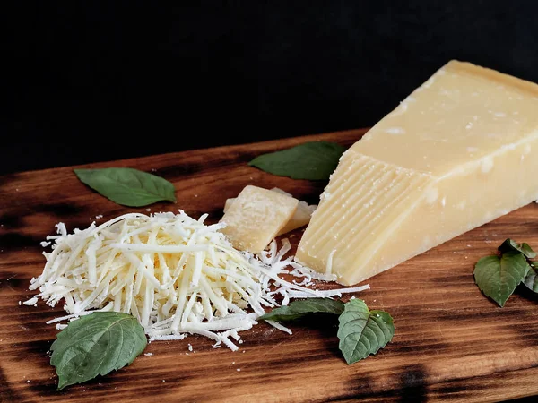 A piece of aged Parmesan cheese with fresh basil leaves. Shot from the top, isolated with a cutting board on a blackbackground