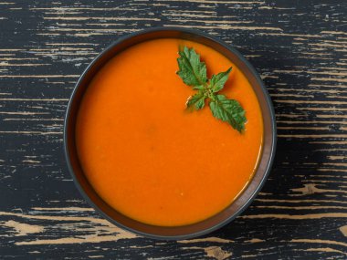 Taze domates, otlar ve zeytinyağı ile Domates çorbası, siyah taş arka plan üzerinde fesleğen.