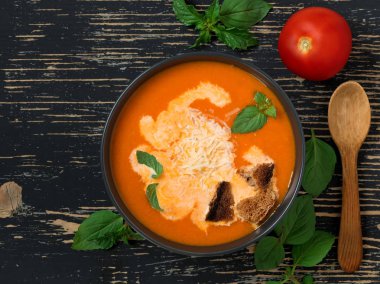 Taze domates, otlar ve zeytinyağı, fesleğen ve ekmek dilimleri ve siyah ahşap arka plan üzerinde kremso ile Domates çorbası.