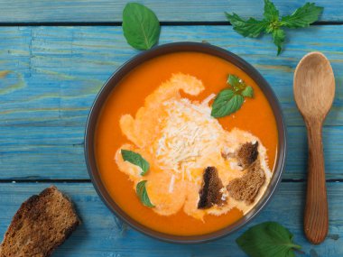 Taze domates, otlar ve zeytinyağı, fesleğen ve ekmek dilimleri ve mavi arka plan üzerinde kremalı sos ile Domates çorbası.