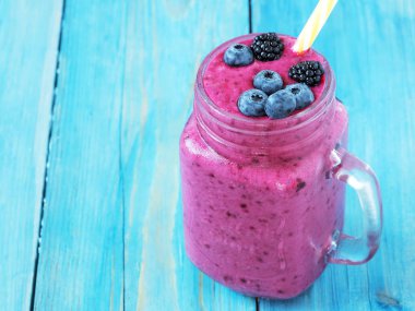 Taze çilek ve muz ile smoothies: süt, böğürtlen, siyah frenk üzümü, yaban mersini. Mavi ahşap arka plan.