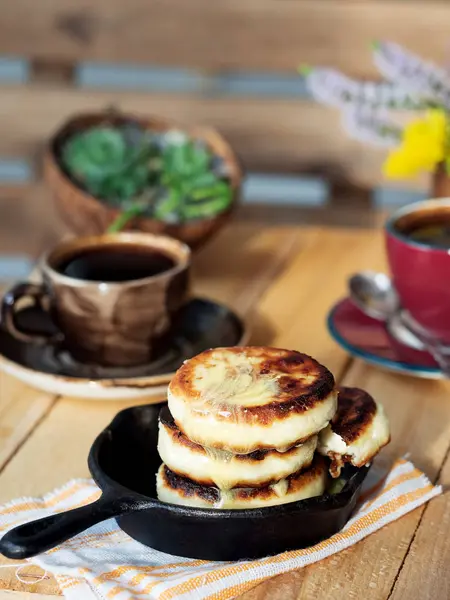 Cheesecakes located on a small frying pan. In the background is a cups of espresso and a bouquet of flowers. Located on a wooden brawn board. Partial focus. — Stock Photo, Image