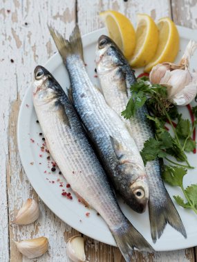 Taze kefal beyaz bir tabakta. Deniz balığı. Baharat, biber, limon. Beyaz ahşap vintage arka plan üzerinde yer almaktadır. Yukarıdan görüntüle.