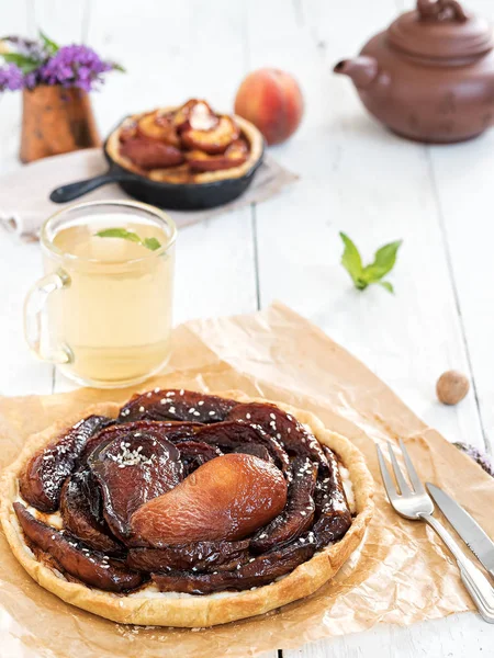 Summer pear cake on a white wooden vintage background. In the background is a cup of tea, chaynmk, peach pie, mint leaves and a bouquet of wildflowers. Close-up. — Stock Photo, Image