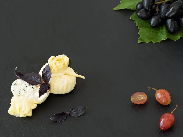 Сыр Сулугуни с рикотто расположен на черной каменной тарелке, рядом с ягодами винограда и кучей спелых винограда на листе. Черный камень фон. Вид сверху . — стоковое фото