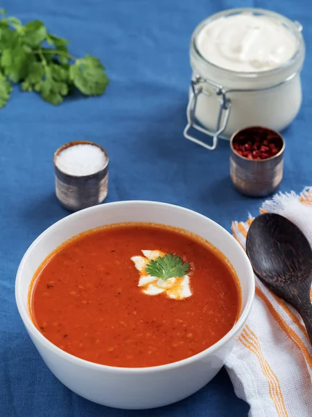 Taze domates çorbası. Mevsimlik yaz yemeği. Mavi keten bir masa örtüsü üzerinde yer almaktadır. Yakınlarda beyaz pamuklu bir peçeteye bir kaşık yatıyor. Soslu ekmek. Close.