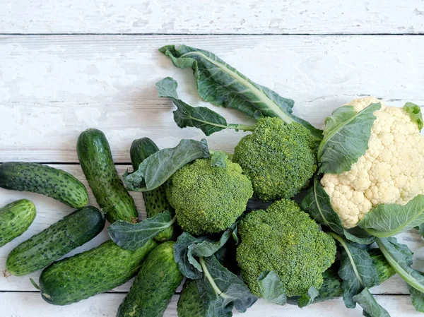 Fresh cauliflower, spinach and cucumbers. Harvesting. Seasonal vegetables. Vegetables are located on a wooden white background. Top view. Free space for text.