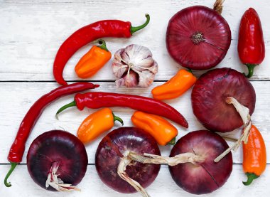 Taze kırmızı biber, kırmızı biber, kırmızı soğan, sarımsak. Baharatlar beyaz ahşap bir arka plan üzerinde düzenlenmiştir. Üstte görüntü.