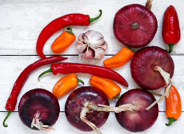 Taze kırmızı biber, kırmızı biber, kırmızı soğan, sarımsak. Baharatlar beyaz ahşap bir arka plan üzerinde düzenlenmiştir. Üstte görüntü.