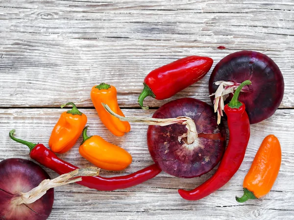 Taze kırmızı biber, kırmızı biber, kırmızı soğan gri ahşap arka plan üzerinde yer almaktadır. Üstte görüntü.
