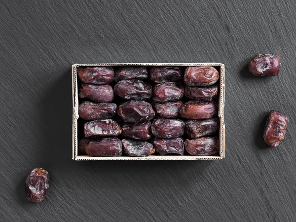 Oriental dates in a cardboard box on a black stone background, three dates next to the box. Top view. — Stock Photo, Image