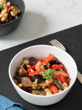 Masada lezzetli haşlanmış patlıcan ve haşlanmış fasulye ve kırmızı biber, kişniş bir prig ile süslenmiş yemekler vardır. Siyah beyaz tabaklar, siyah beyaz arka plan. Close.